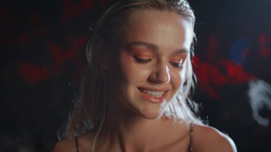 Baştan çıkarıcı kız gece kamerayla flört ediyor. Gülümseyen sarışın, güzel dudakları ısıran, projektör ışıklı portrede poz veren. Çekici, modaya uygun, dik dik bakan bir lens. Siyah arka planda şehvetli genç bir kadın..