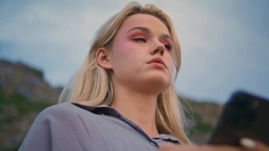 Akıllı telefon mesajını Mountain Cliff 'te yakın plan çekimde kullanan bir kadın. Seyahat haftasonu açık havada mesajlaşan ciddi bir kız. Endişeli sarışın bayan bulutlu gökyüzünde daktilo okuyor..