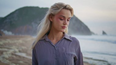 Günbatımının tadını çıkaran düşünceli bir kadın okyanusa yakın çekim yapıyor. Gülümseyen sakin kız kameraya bakıyor ve tropik ada sahillerinde rüya görüyor. Serene güzel sarışın tatildeki yaz dalgalarını düşünüyor. Deniz manzaralı kadın konsepti