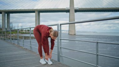 Fitness kızı şehir körfezinde ayakkabı bağlıyor. Şehir koşucusu sabahki kardiyo antrenmanına hazırlanıyor. River Side Köprüsü 'nde spor ayakkabı eğitimi alan güzel bir kadın. Aktif spor giyim yaşam tarzı konsepti.