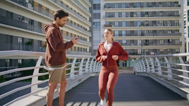 Beden eğitimi koçu zamanlayıcı kadın sabahları koşuyor. Sonuçları tartışan mutlu sporcular. Modern şehir köprüsünde maratondan önce enerjik formda koşucu kız dayanıklılık eğitimi veriyor. Spor yaşam tarzı belirleme