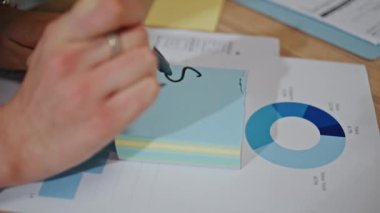 Bir kadın çalışma odasındaki yakın çekimde notlar alıyor. Ahşap ofis masasındaki etiket hesaplama satışları hakkında yazı yazan kimliği belirsiz yönetici kadın. İş teklifini not eden isimsiz bir iş kadını