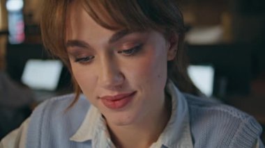 Gülümseyen genç yönetici e-posta okuyan bayan akşam işyerindeki fotoğrafa bakıyor. Geç saatte çalışan işkadını ofis kapanışı. Karanlık iç mekanda poz veren mutlu kadın. Pozitif kız yüzü