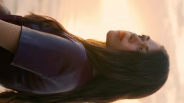 Gün batımında gökyüzünde romantik bir kadının portresi. Resimli okyanusun önünde poz veren rüya gibi model kitabı dikey olarak yakın plan tutuyor. Deniz manzaralı, uzun saçlı, sakin bir kız. Dinlenme kavramı