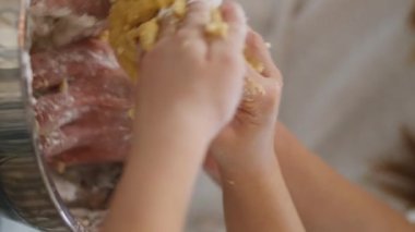 Anne kızı evde hamur yoğururken dikey çekim yapıyor. Bilinmeyen aile açık mutfakta kek pişiriyor. Anonim bir çocuk annesine pasta yapıyor. Kadın parmakları kasede çalışıyor.