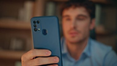 Ciddi bir adam akıllı telefondan SMS okuyor. Evdeki oturma odasını kapatın. Gece geç saatlerde cep telefonu ekranına odaklanmış genç bir işadamı. Yakışıklı adam karanlık ofiste alışveriş uygulamasına bakıyor..