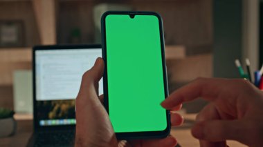 Girişimci, krom anahtarlı cep telefonu araklıyor ve yakın çekimde online alışveriş yapıyor. Erkek eli yeşil ekran cep telefonuna dokunuyor akşam ofisinde sosyal medyada geziniyor. Bilinmeyen adam model aygıtı