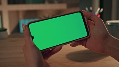 Girişimci videosu, karanlık ofisteki Chroma Key cep telefonunu arıyor. Yatay yeşil ekran akıllı telefon kullanan tanınmayan bir iş kadını. Kadın elleri akşam evde cep telefonlarını tutuyor..