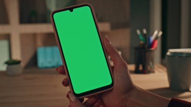 Kadın elleri evde yeşil ekran cep telefonu tutuyor. Kapatın. Tanımlanamayan kadın kullanıcı akıllı telefondan sosyal medya içeriğini izliyor. İş kadını krom anahtar cep telefonunda SMS okuyor.