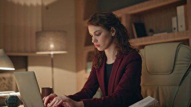 Karanlık, modern iş yerinde dizüstü bilgisayarı daktilo eden odaklanmış bir iş kadını. Belgelere bakarak proje üzerinde çalışan ciddi bir girişimci kadın. Genç bayan yönetici gece iş belgelerini düşünüyor..