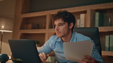 Kağıtları inceleyen mutlu iş adamı karanlık ofiste mali sonuçları kutluyor. Duygusal adam elinde dizüstü bilgisayarla muzaffer bir evet hareketi yapıyor. Başarıyı kutlayan yatırımcı