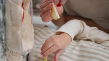 Kadın çocuk elleri elmayı dikey olarak pişirme şekline sokuyor. Tanınmayan aile, hafif mutfakta birlikte turta hazırlıyor. Bilinmeyen bir anne kızıyla birlikte gelecekteki tatlıyı süslemeye yardım ediyor.