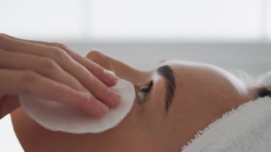 Banyoda yüz temizleyen muhteşem kadın dikey olarak yakın plan. Sabah rutinini yapan, pamuklu pedlerle cildini ovuşturan bir kız. Havlu kafalı tatmin olmuş kadın evde duş aldıktan sonra kirliliği temizliyor.