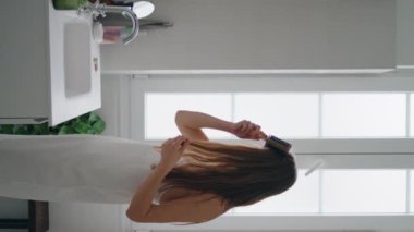 Dikey olarak ayna yerinde saç tarayan çekici bir model. Kendine güvenen bir kadın banyoda saç stili yapıyor. Kız her sabah evde rutin şeyler yapmaya hazırlanıyor. Günlük güzellik prosedürleri