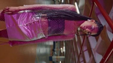 Güzel bir kadın, neon yeraltı otoparkında dikey olarak dikey çekim yapıyor. Kahverengi derili, kamera görüntülü portre. Arka planda poz veren kendinden emin genç bir kız. Moda güzelliği