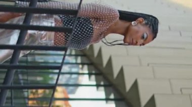Merdivenlerden inen şık bir model modern bina dikey meleği. Dreadlocks Afro-Amerikalı kadın merdivenlerde tek başına sakin bir gezinti yapıyor. Modaya uygun esmer kız aşağı inip şehri geziyor.