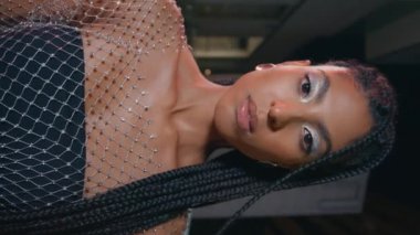 Yaratıcı makyöz Afrikalı kadın dikey olarak gece fotoğrafına bakıyor. Afro saç stili, ciddi esmer, akşam fotoğrafında poz veriyor. Siyah tenli, şehvetli kadın şehir merkezinde tek başına objektife bakıyor.