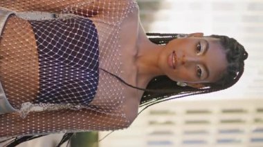 Kozmik Afrikalı kadın güneşli şehir merkezindeki dikey video resmine bakıyor. Dehşet saçan, modaya uygun makyajlı kadın, yaz şehrinin yakın çekimlerinde poz veriyor. Muhteşem model mercek doğrudan yakınlaştır.