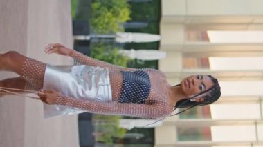 Seksi esmer tek başına yeşillik mahallesinde dikey olarak geziniyor. Şık giyinmiş, çantalı, boş sokaktan geçen mutlu Afro-Amerikan kadını. Moda mankeni kız sokakta yürüyor.