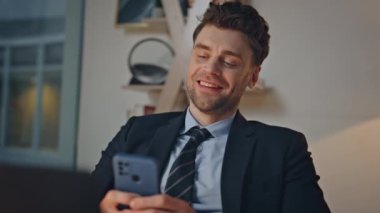 Neşeli bir ofis çalışanı cep telefonuyla mesajlaşıyor. Ofis içi akşam yakın çekim yapıyor. Gülümseyen yönetici iş yerindeki akıllı telefondan sosyal medya içeriğine göz atıyor. Neşeli çalışan cep telefonunda mesaj atıyor