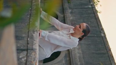 Korkuluklara eğilen şehvetli kız terk edilmiş kalenin balkonunda. Huzurlu çekici kadın akşam güzelliğine bakıyor. Eski taş kale terasında dikey videoda duruyor. Tasasız bayan, ortaçağ sarayının tadını çıkarın..