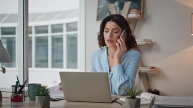Çağdaş ofisteki iş belgelerini araştıran ciddi bir kadın. Profesyonel iş kadını akıllı telefondan konuşuyor. Masasında dizüstü bilgisayarla oturuyor. Meşgul kadın CEO telefon görüşmeleri yapıyor..