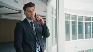 Modern ofis koridorunda ciddi bir iş adamı cep telefonuyla konuşuyor. Yönetici, pencere kenarındaki şirket binasının yanındaki akıllı telefondan önemli görevleri tartışıyor. Profesyonel takım elbiseli, telefon görüşmesi yapıyor.