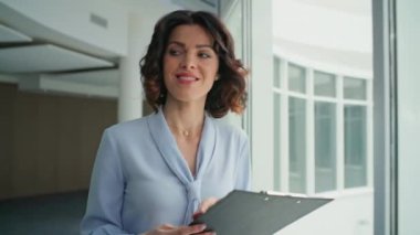 Gülümseyen patron modern ofiste dokümanları gözden geçiriyor. Kendine güveni olan kadın yönetici iş anlaşmasıyla iş arkadaşını selamlıyor. Mutlu kadın yönetici koridor penceresinin yanında kağıtlara bakıyor..