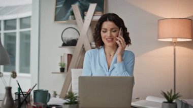 Başarılı girişimci akıllı telefonu arıyor ofis masasında dizüstü bilgisayar arıyor. Kendine güvenen bir bayan yönetici iş yerinde cep telefonuyla iş belgelerini tutuyor. Gülümseyen iş kadını konuşuyor.