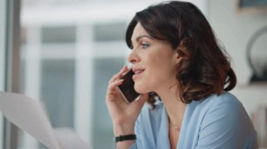 Memnun olmayan CEO, ofis masasında otururken evrakları kapatıyor. Ciddi bir iş kadını cep telefonuyla konuşuyor çalışma alanında rapor veriyor. Kadın patron, akıllı telefon konuşmasından memnun değil.