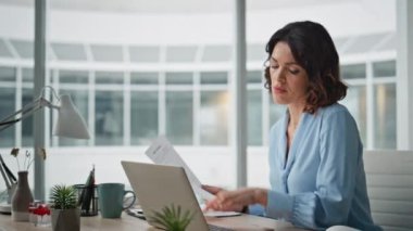 Modern ofis iç çekimlerinde duran uzman görünümlü belgeler. Odaklanmış iş kadını laptopta çalışırken gazete okuyor. Çağdaş şirket çalışma alanında evrak işleriyle uğraşan zeki bir kadın..