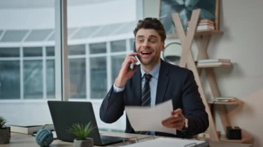 Gülümseyen işadamı akıllı telefondan konuşuyor. Ofis masasındaki belgeleri yakından inceliyor. Başarılı bir yönetici, şirket işyerindeki ortakları çağıran kağıtları gözden geçiriyor. Konuşan yönetici cep telefonu daktilo dizüstü bilgisayarı.