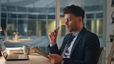 Şirket çalışanı ofis masasındaki evrak işlerine odaklanmış, derin düşüncelere dalmış. Genç profesyonel okuma kağıtları geç saatlere kadar çalıştığını gösteriyor. İşadamı, belgeleri konsantrasyonla analiz ediyor