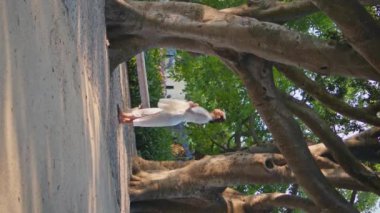 Romantik kız beyaz eşarba sarılmış parkta dinleniyor. Hayalperest kadın, geniş yeşil ağaçların altında dikey doğa güzelliğine bakıyor. Yalnız, kaygısız bayan hafta sonu açık havada yaz bahçesinin tadını çıkar.