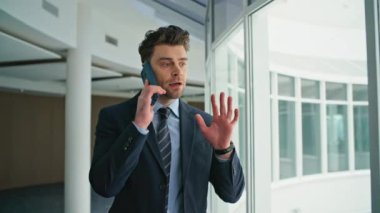 Öfkeli yönetici koridordaki panoramik pencereleri kapatmayı bitirdi. Sinirli iş adamı iş sorununu açıklayan akıllı telefondan tartışıyor. Sinirli adam telefonu kapattı. Duygusal olarak..