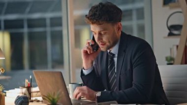 Ofis masasında cep telefonuyla konuşan geç çalışan bir işçi ciddi bir ifadeyle yakın çekimde. Çok çalışan yönetici, bilgisayarla telefon görüşmesi yapıyor. Endişeli yönetici iş yerindeki iş görüşmesine odaklanıyor.
