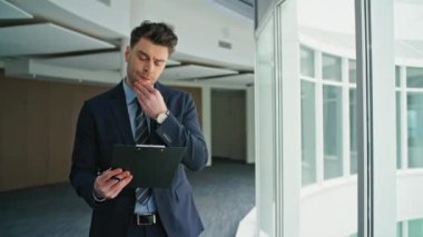 Ofis koridorlarında dokümanları okuyan düşünceli bir yönetici. Yakın plan. Profesyonel iş adamı iş belgelerini hazırlıyor. Ciddi girişimci belgelere odaklandı.