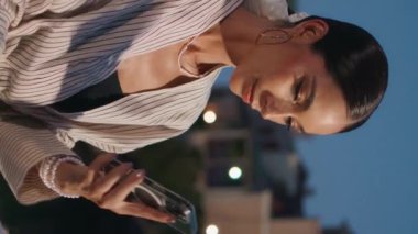 Modayı takip eden iş kadını, deniz kenarındaki alacakaranlık dikey görüntüsünü kapatıyor. Gülümseyen mutlu bir kadın, akıllı telefonlardan bahsederek akşam sahil şehrinde oturuyor. Gülümseyen kız arkadaşça telefon konuşmalarından hoşlanıyor