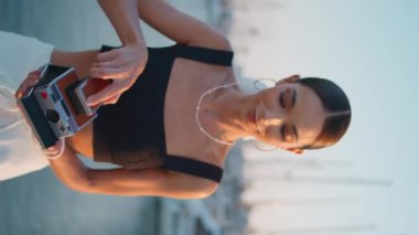 Mutlu kadın fotoğraf makinesini akşam iskelesinde dikey çekime ayarlıyor. Rahat kız deniz manzarası fotoğrafı çekmek için retro kamera kullanıyor. Rıhtımda lüks yatların fotoğraflarını çeken zarif genç bir bayan.