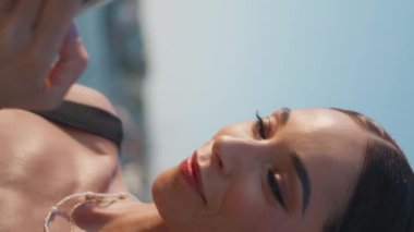 Yaz mevsiminde deniz kenarında dikey görüntüde mesaj yazan rahat bir kız. Güneşli toprak setinde akıllı telefondan mesaj atan bronz tenli bir kadın. Moda bayan turist gezme mobil uygulaması deniz kıyısında dinleniyor.