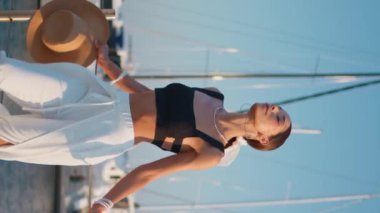 Rıhtımda poz veren sakin bir kadın dikey olarak yaz rüzgarının tadını çıkarıyor. Öndeki beyaz yatlarda durup tatilde dinlenen muhteşem bir manken. Zarif kız gözlerini kapatıp iskelede yüzünü güneş ışığına çıkarıyor..