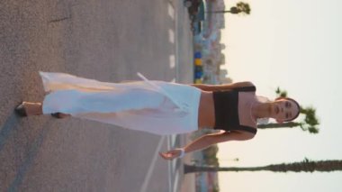 Şatafatlı kız gün batımında dikey yolda yürüyor. Muhteşem bir manken yaz akşamı asfalt yolda geziniyor. Kendine güvenen zarif bir kadın tropikal sokaklarda tek başına dolaşıyor. Modayı takip eden bayan kamera..