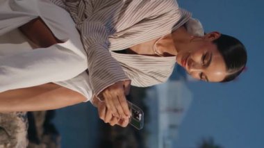 Şık bir gezgin, gece sahil kasabasında dikey olarak akıllı telefon kaydırıyor. Zarif bir kadın cep telefonu ekranına bakıyor ve gülümsüyor. Quay caddesinde cep telefonu uygulamasına bakan mutlu kız