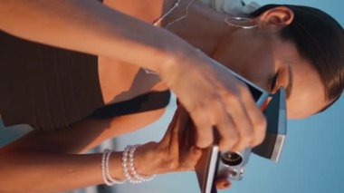 Kız turist, güzel bir akşam fotoğrafı çekiyor. Gülümseyen esmer kadın retro kamerayla resimli iskele manzarası çekiyor. Okyanus kıyısında fotoğraf çeken mutlu kadın gezgin..