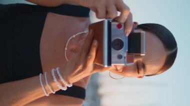 Yaz tatilinde fotoğraf çeken bir kadın. Dikey video çekimi. Gülümseyen rahat turist kız retro kameraya bakıyor ve deniz manzarası yapıyor. Kaygısız kadın gezgin doğayı fotoğraflıyor.