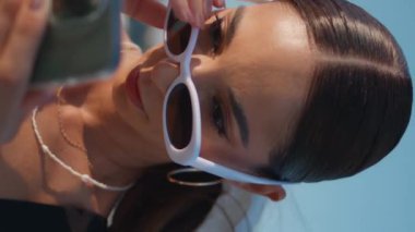 Sahildeki modaya uygun bayan mesajlaşması. Güneş gözlüğünü dikey olarak çıkartıyor. Güzel, mutlu kadın güneşli deniz kıyısında akıllı telefon ekranına bakıyor. Sahilde cep telefonundan mesaj okuyan bir kız..