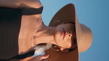 Öndeki yat direğinde poz veren şık şapka modeli set dikey görüntüsünde dikey çekim yapıyor. Mavi gökyüzünde duran sosyetik kadının portresi. Muhteşem kendine güvenen kız kameraya bakıyor yaz tatilinin tadını çıkarıyor