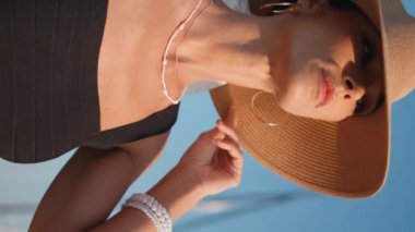 Hasır şapkalı kız güneşli doğada dinleniyor dikey meleğin yakın çekimi. Yaz tatilinde yelken direğinde poz veren zarif bronzlaşmış kadın portresi. Rıhtımdaki lüks başlıklı modacı.