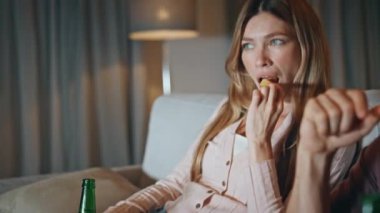 Kadın, cam kaseden atıştırmalık bir şeyler alıyor. Kaygısız kadın arkadaşlar ellerinde bira şişeleriyle birlikte televizyon izliyorlar. Rahat eşler komedi filminin tadını çıkarıyorlar.