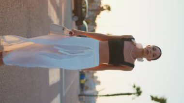 Günbatımı yolunda yürüyen zengin bir iş kadını son moda kıyafetlerle dikey çekim yapıyor. Kendine güveni tam esmer bir kadın yaz akşamı yola çıkıyor. Modayı takip eden başarılı bayan güzel günbatımının tadını çıkarıyor..